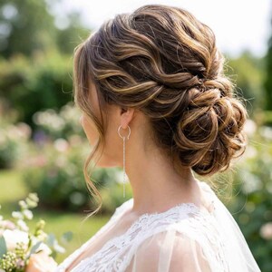 May include: A woman with a sophisticated hairstyle, wearing silver chain earrings. The hair is styled in a low bun with loose waves. The woman is wearing a white lace dress, with a blurred green background.
