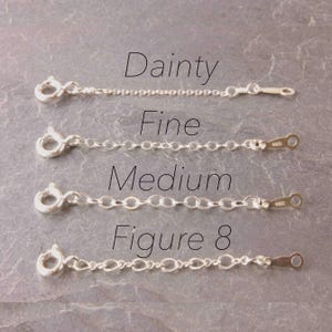 May include: Four silver chain extenders labeled "Dainty", "Fine", "Medium", and "Figure 8". Each extender has a clasp on one end and a small loop on the other. The chains are displayed on a textured, gray surface.