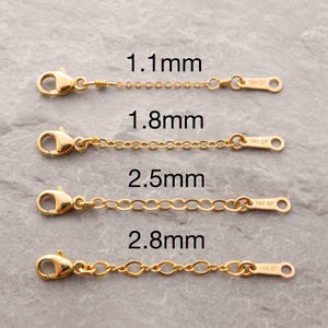 May include: Four gold-toned jewelry extender chains with lobster claw clasps, labeled 1.1mm, 1.8mm, 2.5mm, and 2.8mm. Each chain features a small flat tag stamped with 14K GF, indicating gold-filled material, arranged vertically in increasing size.
