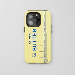 May include: A pale yellow phone case featuring a blue graphic design that mimics a butter wrapper. The text reads SALTED BUTTER, GRADE AA, and includes a measurement scale with markings from 1 TBSP to 9 TBSP and 1 CUP.