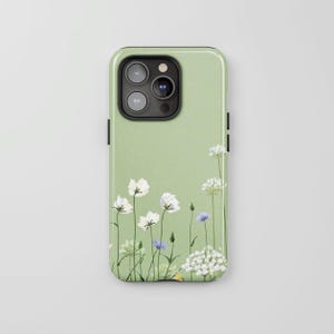 May include: A sage green smartphone case featuring a delicate botanical illustration of white and light blue wildflowers with thin green stems. The design covers the back of the case, which has a black camera module cutout at the top left corner.