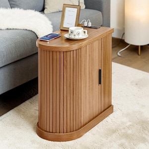 May include: A wooden side table with a curved design and vertical slat detailing. The table has a light brown finish and a small black handle on the door. A photo frame, a teacup, and a smartphone are on the top surface.