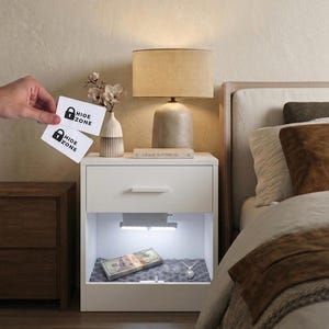 May include: A white bedside cabinet with a hidden, illuminated compartment. Inside, there's a stack of banknotes, jewellery, and a grey foam insert. Two cards with "HIDE ZONE" text are held above the cabinet.