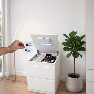 May include: A white nightstand with a hidden compartment, open to reveal cash, jewelry, and a watch. The top is open with a light and a small lock. Two cards with "HIDE ZONE" are held in front of the nightstand.
