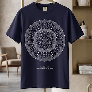 Op de afbeelding: Een marineblauw t-shirt met korte mouwen en een groot, wit, ingewikkeld geometrisch cirkelpatroon van onderling verbonden lijnen en knooppunten. Onder de afbeelding staat de tekst: PHASE BOUNDARY. Stability exists in the nodes.