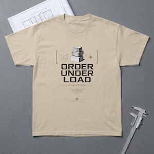 Puede incluir: Una camiseta beige con el texto "ORDER UNDER LOAD" y un gráfico de bloques apilados. La camiseta también presenta el texto "structure holds" y un pequeño diseño. Un plano y un calibrador están en el fondo.
