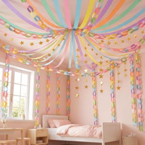 May include: A ceiling decoration featuring pastel-coloured paper chain garlands in pink, yellow, blue, and green, radiating from the centre. Gold star-shaped ornaments hang vertically from the ceiling, interspersed with the paper chains.