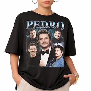 May include: Black t-shirt featuring a collage of images of Pedro Pascal, with the name "PEDRO" in a metallic blue font. The design includes various portraits of the actor, creating a vintage-style graphic.