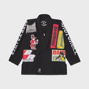 May include: Black Jiu-Jitsu gi with multiple patches. Patches include the text "BornXRaised", "Shoyoroll", "BXR Los Angeles", and various graphics. The gi has white text on the sleeves and a small logo near the bottom.