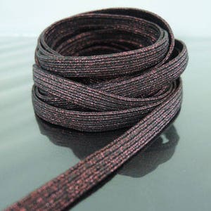 Puede incluir: Un rollo de cinta elástica negra con un fino acabado de purpurina roja. La cinta mide aproximadamente 1,2 cm de ancho.