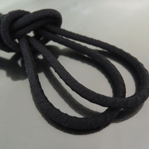 Può includere: Un primo piano di un cordoncino elastico nero, annodato. Il cordoncino è spesso e sembra essere fatto di un materiale morbido ed elastico.