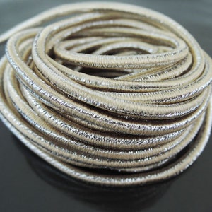 May include: A close-up of a roll of silver metallic elastic cord. The cord is approximately 6mm wide and has a subtle ribbed texture.