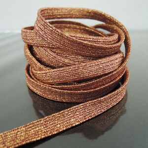 May include: A spool of brown and gold elastic cord with a shimmery finish. The cord is coiled and ready to be used for crafts or sewing projects.