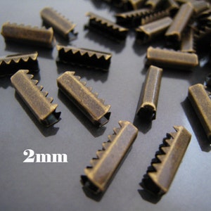 Könnte beinhalten: Nahaufnahme einer Reihe von 2 mm großen antiken Messing-Schiebeschließen. Die Schließen sind klein und haben einen gezahnten Rand.