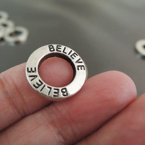 May include: Silver charm with the word "BELIEVE" engraved around the edge.