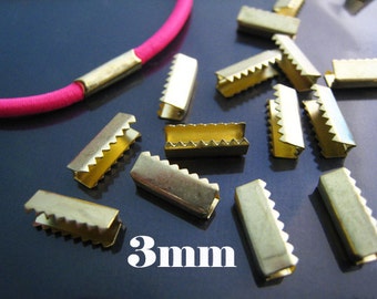 May include: A close-up of 3mm gold-coloured metal slider buckles. The buckles have a serrated edge and are arranged on a dark blue surface.