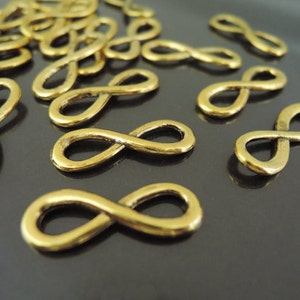May include: A group of gold-colored infinity symbol charms. The charms are scattered on a dark surface.