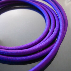 May include: A close-up of a coil of purple elastic cord. The cord is smooth and shiny, and it is coiled in a tight spiral.