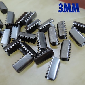 Puede incluir: Un montón de hebillas deslizantes de metal plateado de 3 mm. Las hebillas tienen un borde dentado y están diseñadas para ser usadas con correas o cintas.