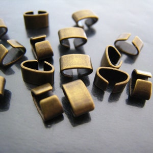 Op de afbeelding: Een groep van 15 antieke gouden metalen sluitingen, ook wel bekend als koorduiteinden, voor het maken van sieraden. De sluitingen zijn klein en hebben een eenvoudig ontwerp.