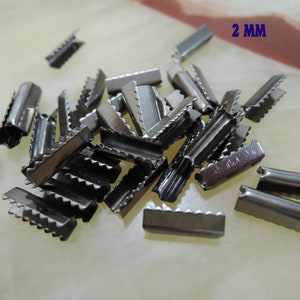 May include: A pile of silver metal slider buckles, each measuring 2 mm in width. The buckles have a serrated edge and are designed to be used for attaching straps or cords.