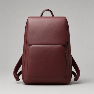 Puede incluir: Una mochila de color burdeos intenso con un acabado liso y mate. La bolsa cuenta con una solapa superior grande que cubre el compartimento principal, un bolsillo vertical con cremallera en el panel frontal, un asa superior y dos correas ajustables.