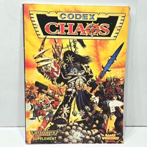 May include: A Codex Chaos supplement book with a vibrant cover featuring a warrior in black armor wielding a blue sword. The cover has the text "CODEX CHAOS" and "WARHAMMER 40,000 SUPPLEMENT" against a yellow and orange background.