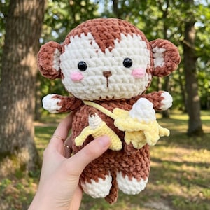 May include: A handmade crochet monkey doll with brown and white fur, black eyes, and pink cheeks. The monkey has a yellow banana accessory. The doll is approximately 8 inches tall.