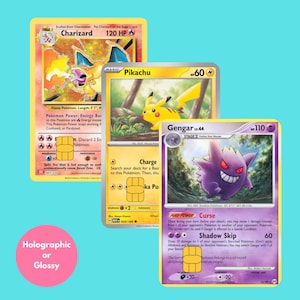 May include: Three trading cards featuring Charizard, Pikachu, and Gengar with gold chip overlays. The Charizard card is orange, the Pikachu card is yellow, and the Gengar card is purple. A pink circle in the corner contains the text Holographic or Glossy.