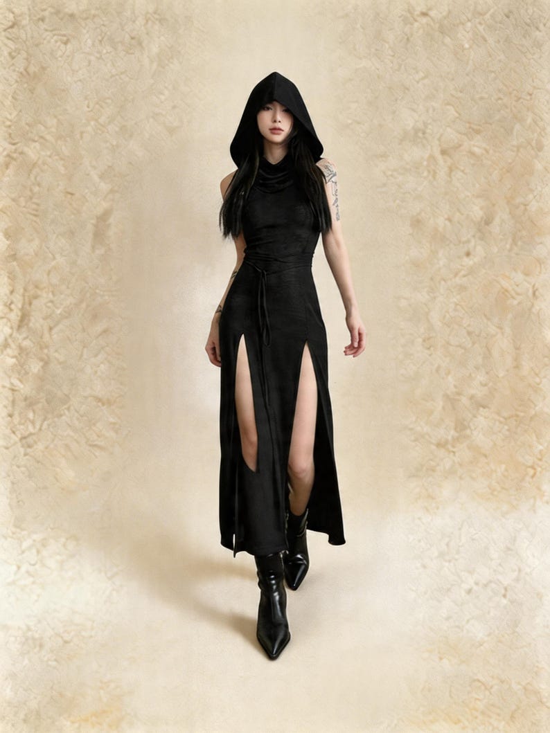Pode incluir: Vestido preto com capuz e fendas laterais altas. O vestido sem mangas tem cintura marcada e &eacute; usado com botas pretas de bico fino. O fundo &eacute; bege neutro.