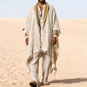 May include: A cream-colored, textured poncho with a fringed hem, worn over a white shirt and pants. The outfit includes a brown collar and cuffs. The person is standing in a desert setting, wearing tan shoes.