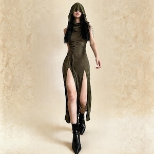 Pode incluir: Vestido verde-oliva com capuz, fendas altas e cintura com cord&atilde;o. O vestido &eacute; combinado com botins pretos. A modelo caminha para a frente sobre um fundo neutro. O vestido &eacute; sem mangas.