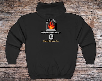 May include: Black hooded sweatshirt with a white graphic featuring a flame and cross design, the text "TheFirePlace.Church", a cross icon, and the words "Glow Grow Go". The sweatshirt is displayed on a wooden surface.