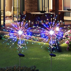 May include: Two solar-powered garden lights featuring starburst-shaped heads with thin, radiating wires tipped with small, glowing multi-colored LED lights. Each light is mounted on a thin metal stake with a black solar panel base at the bottom.