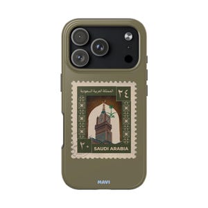 Peut inclure: Coque de téléphone vert olive avec un motif de timbre de l'Arabie Saoudite. La coque présente une image détaillée d'un bâtiment avec une tour d'horloge et le texte "SAUDI ARABIA". La coque a une finition mate et la marque "MAVI" est imprimée en bas.