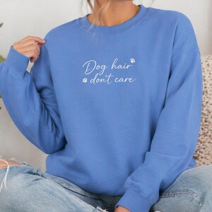 May include: A light blue sweatshirt with the text "Dog hair don't care" in white script. The sweatshirt has a crew neck and long sleeves. A paw print design is next to the text.