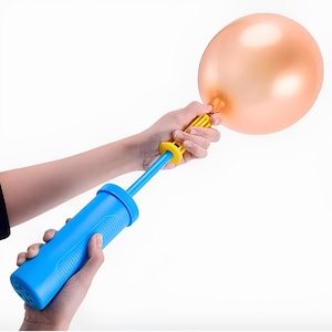 May include: A blue and yellow balloon pump inflating a gold-colored balloon. The pump is held in two hands, with the balloon's neck secured to the pump's nozzle. The pump has a blue body and a yellow handle.