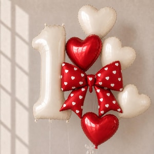 May include: A balloon arrangement featuring a large cream-colored number one balloon, three cream-colored heart balloons, two red heart balloons, and a central red bow balloon decorated with a white heart pattern, all tied together with thin strings.