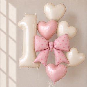May include: A collection of foil balloons featuring a large cream-colored number one, a pink bow balloon with a small heart pattern, and several heart-shaped balloons in shades of cream and soft pink, all attached to thin white ribbons.