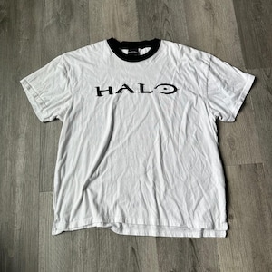 May include: White t-shirt with a black collar and the word "HALO" printed in black across the chest. The shirt has short sleeves and a crew neck. The shirt is made of a soft, comfortable material.