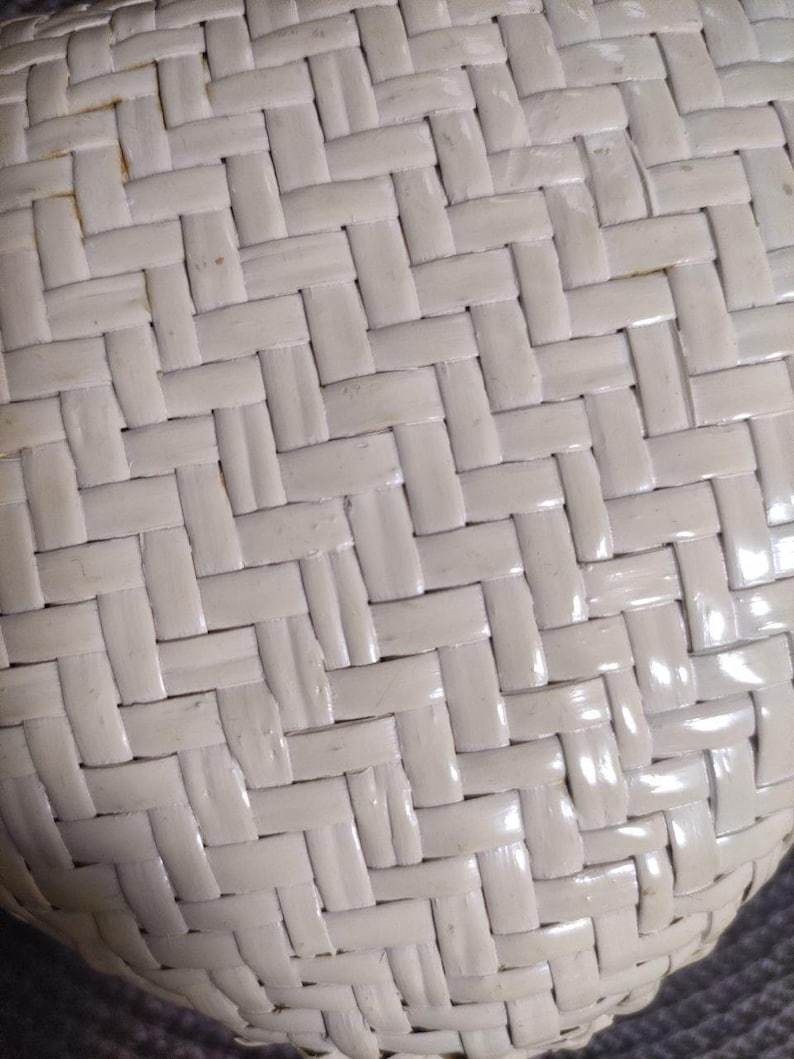 May include: A close-up view of a white woven surface featuring a repeating herringbone pattern. The material consists of flat, smooth strips interlaced in a tight, diagonal configuration, creating a consistent texture across the entire visible area.