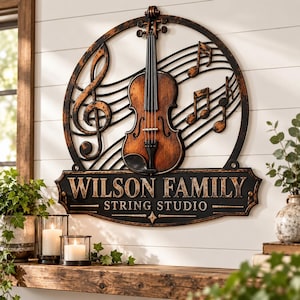 May include: A circular metal wall sign featuring a central violin, musical staff lines, and notes. The sign has a distressed bronze and black finish. Below the circle, a rectangular plaque displays the text WILSON FAMILY STRING STUDIO.