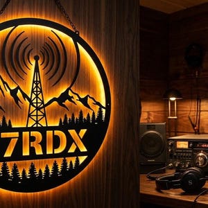 Może przedstawiać: Okrągły szyld ścienny z czarnego metalu z podświetlaną sylwetką wieży radiowej, pasma górskiego i sosen, z tekstem K7RDX umieszczonym centralnie, oświetlonym ciepłym pomarańczowym blaskiem.