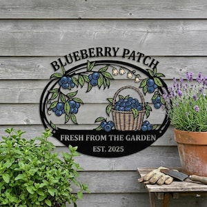 May include: Black metal sign with the words "Blueberry Patch" and "Fresh From The Garden" with a basket of blueberries and foliage. The sign also includes the year "EST. 2025". The sign is mounted on a wooden wall.
