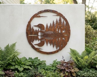 Puede incluir: Una pieza de arte mural circular de metal con un acabado de color óxido. El diseño muestra un colimbo nadando en el agua con su reflejo debajo, rodeado por un denso bosque de pinos. La obra está enmarcada por un borde circular de metal.