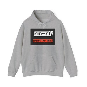 Puede incluir: Una sudadera con capucha gris claro con un bolsillo delantero y una capucha con cordón. La parte delantera de la sudadera con capucha presenta un rectángulo negro con el texto "rm-rf/" en blanco y "(Don't Try This)" en rojo.