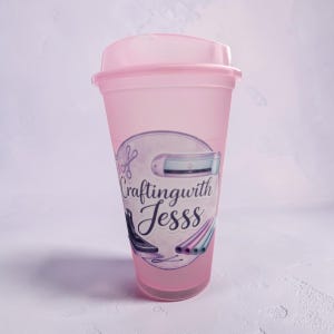 以下が含まれることがあります： ピンク色のプラスチックタンブラーと、お揃いの蓋。 タンブラーには、「Craftingwith Jesss」の文字とクラフトツールの画像が入った円形のグラフィックが描かれています。 このカップは冷たい飲み物用に設計されています。