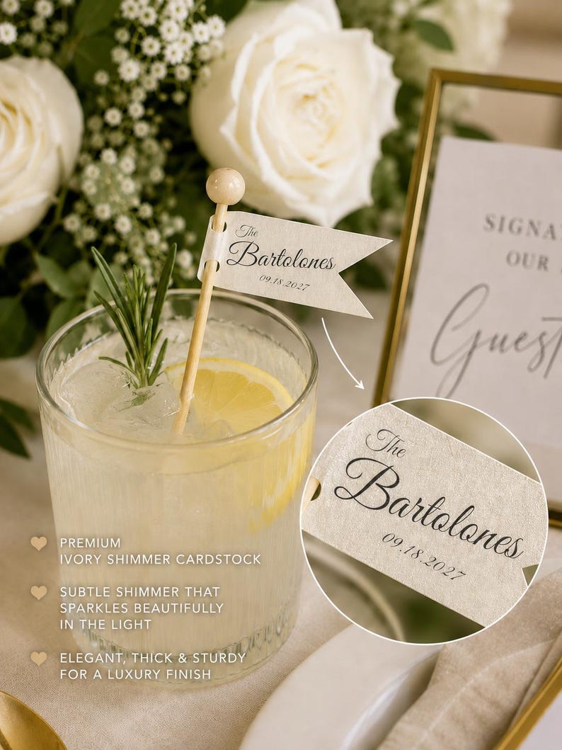 May include: A cocktail stirrer featuring a small, cream-coloured flag made of ivory shimmer cardstock. The flag is printed with the text The Bartolones and the date 09.18.2027. The stirrer is placed in a glass containing a clear liquid, ice, and a lemon slice.