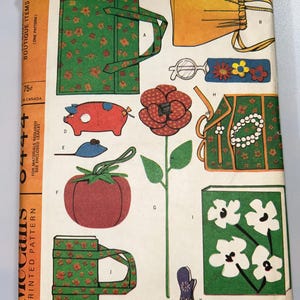 May include: Vintage McCall's printed pattern featuring various boutique items. The cover displays illustrations of a green floral tote bag, a drawstring pouch, a pig, a tomato, a flower, and other accessories. The price is 75¢.