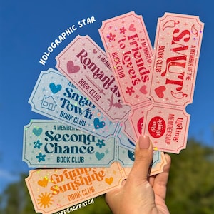 May include: A collection of holographic star-patterned ticket-shaped bookmarks featuring text including Smut Book Club, Friends to Lovers Book Club, Romantasy Book Club, Small Town Book Club, Second Chance Book Club, and Grumpy Sunshine Book Club.
